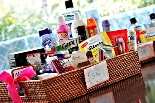 A wicker basket labeled "Hers" filled with various toiletries, medications, and personal care items, placed on a reflective surface.