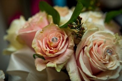 A close-up of pale pink roses with fake diamonds placed in the centers of the blooms, surrounded by green leaves.
