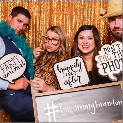 Four people pose in front of a gold sequin backdrop at a photo booth for a wedding, holding props and signs that read "PARTY animal," "happily ever after," and "DON'T TAG THIS PHOTO.