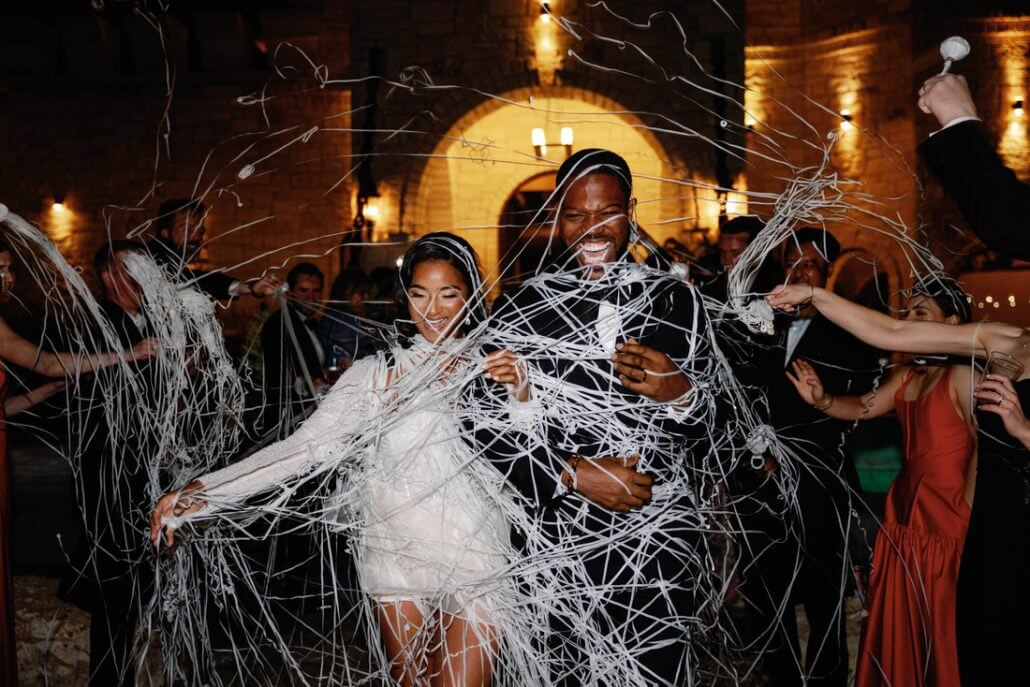 Houston wedding photography by Toast: a bride and groom walk through a crowd as guests spray them with white streamers indoors during a celebration.