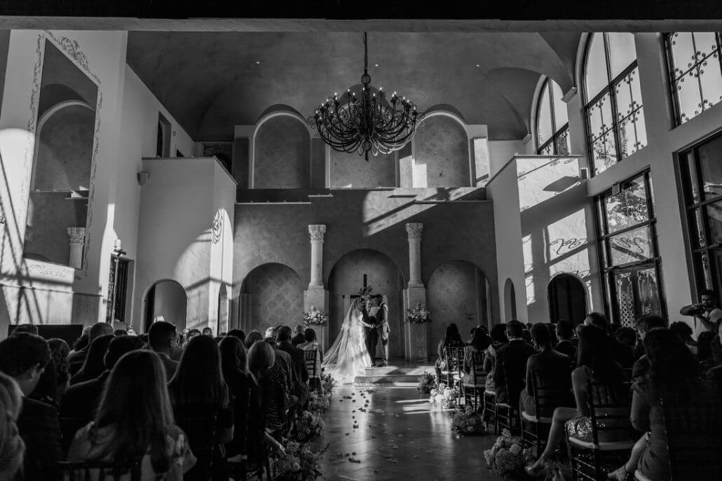 Houston wedding photography by Toast: a bride and groom stand at the altar during a wedding ceremony in a sunlit, elegant chapel filled with seated guests.