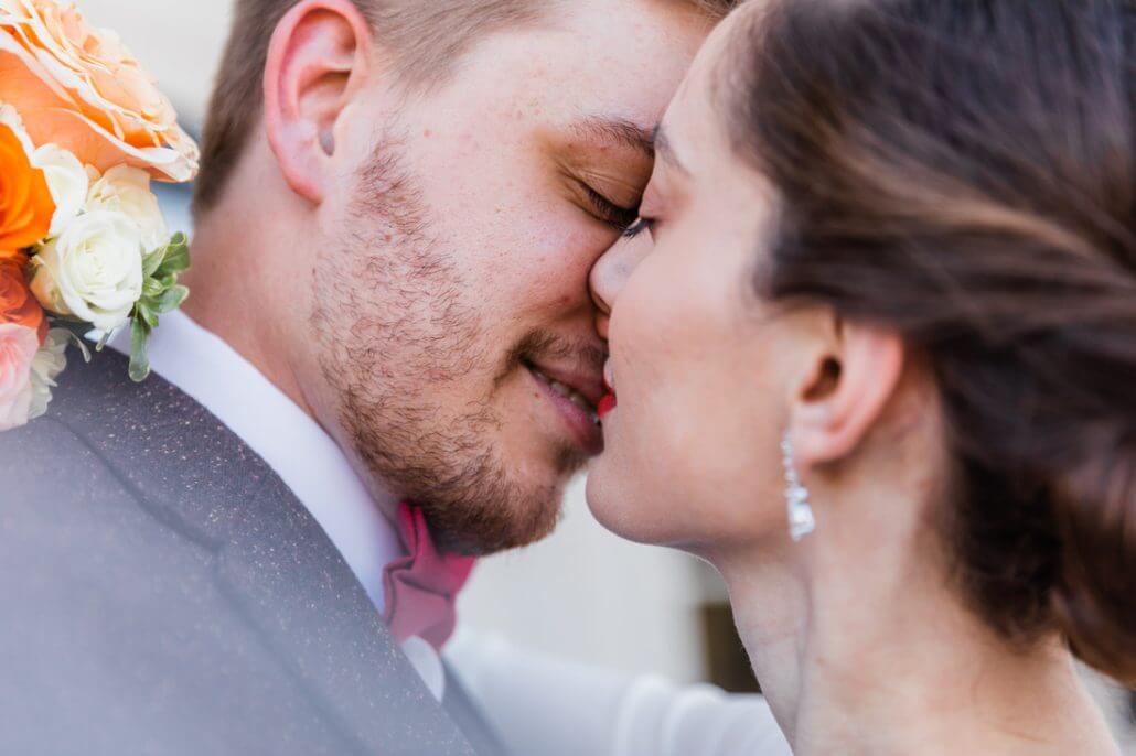 Fort Worth wedding photography by Toast: a close-up of a couple embracing, faces touching closely, with the man smiling and holding a bouquet of orange and white flowers over his shoulder.