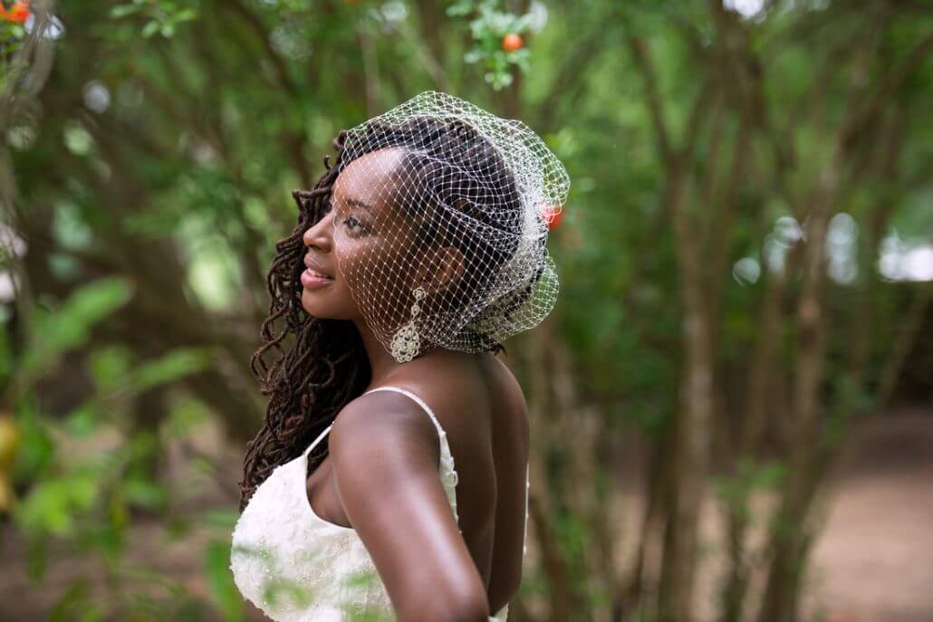 San Antonio wedding photography by Toast: a woman in a white dress and birdcage veil stands outdoors, looking to the side, with greenery in the background.