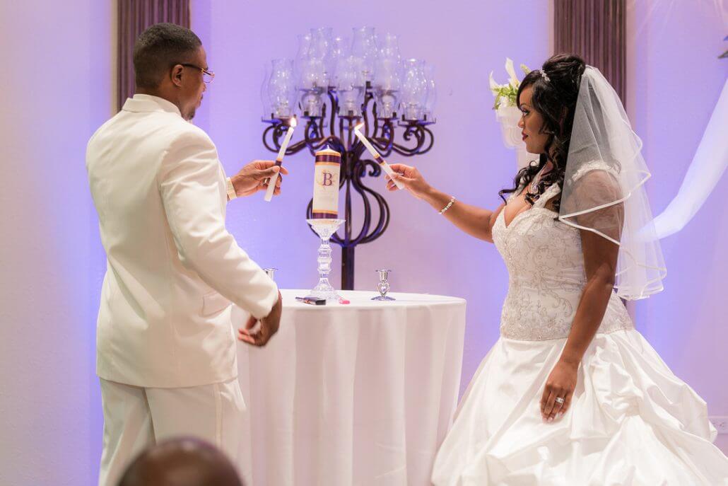 Fort Worth wedding photography by Toast: a bride and groom in white attire light a unity candle together during a wedding ceremony, standing at a small round table.