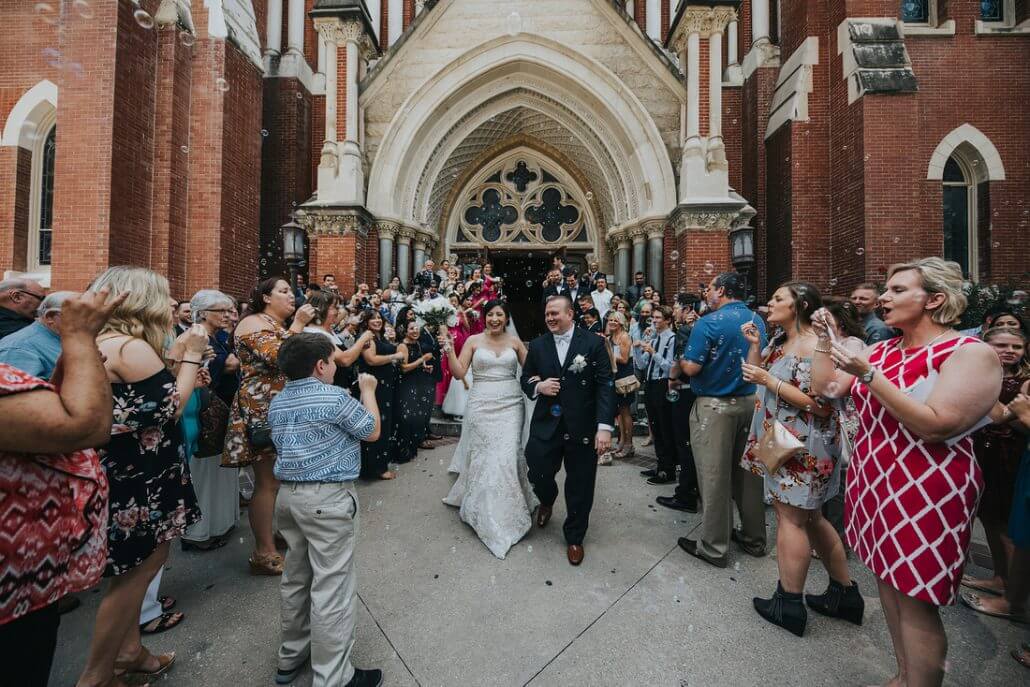 Fort Worth wedding photography by Toast: a bride and groom walk out of a church while guests stand on both sides, applauding and blowing bubbles.
