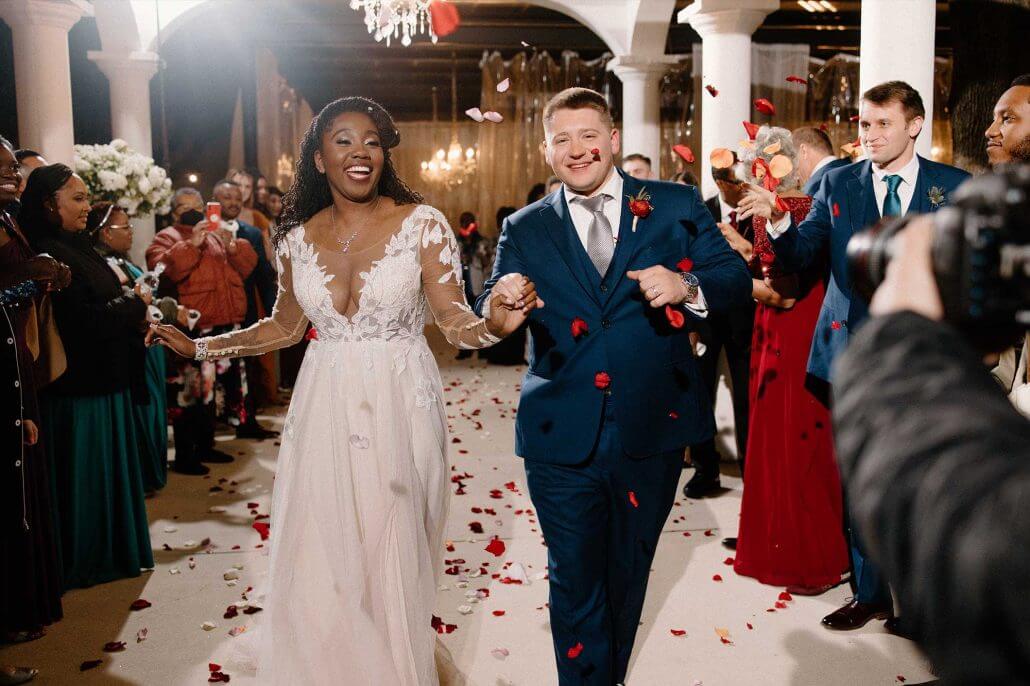 Bride and groom walking hand in hand back up a petal-covered aisle as guests toss rose petals at their Dallas wedding.