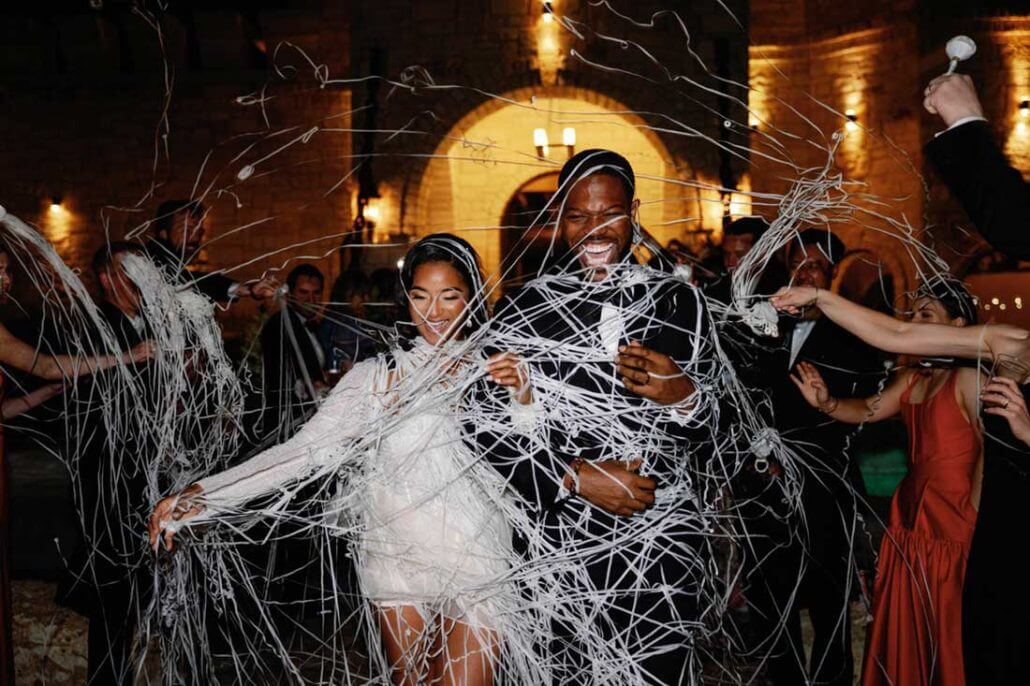 Houston wedding photography by Toast: a bride and groom smile as guests spray them with white streamers at an indoor wedding celebration.