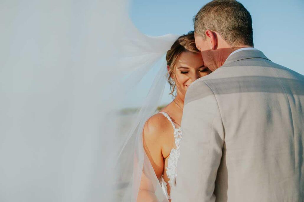 South Texas wedding photography by Toast: a bride and groom stand closely together outdoors, partially covered by the bride's veil, with the bride smiling and eyes closed.