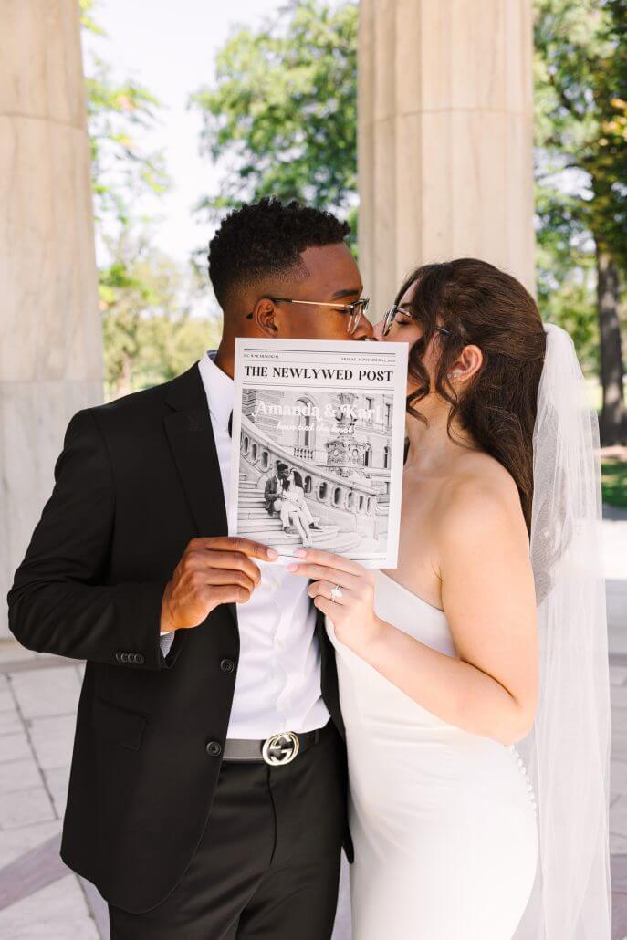 A bride and groom in wedding attire kiss while holding up a newspaper titled 