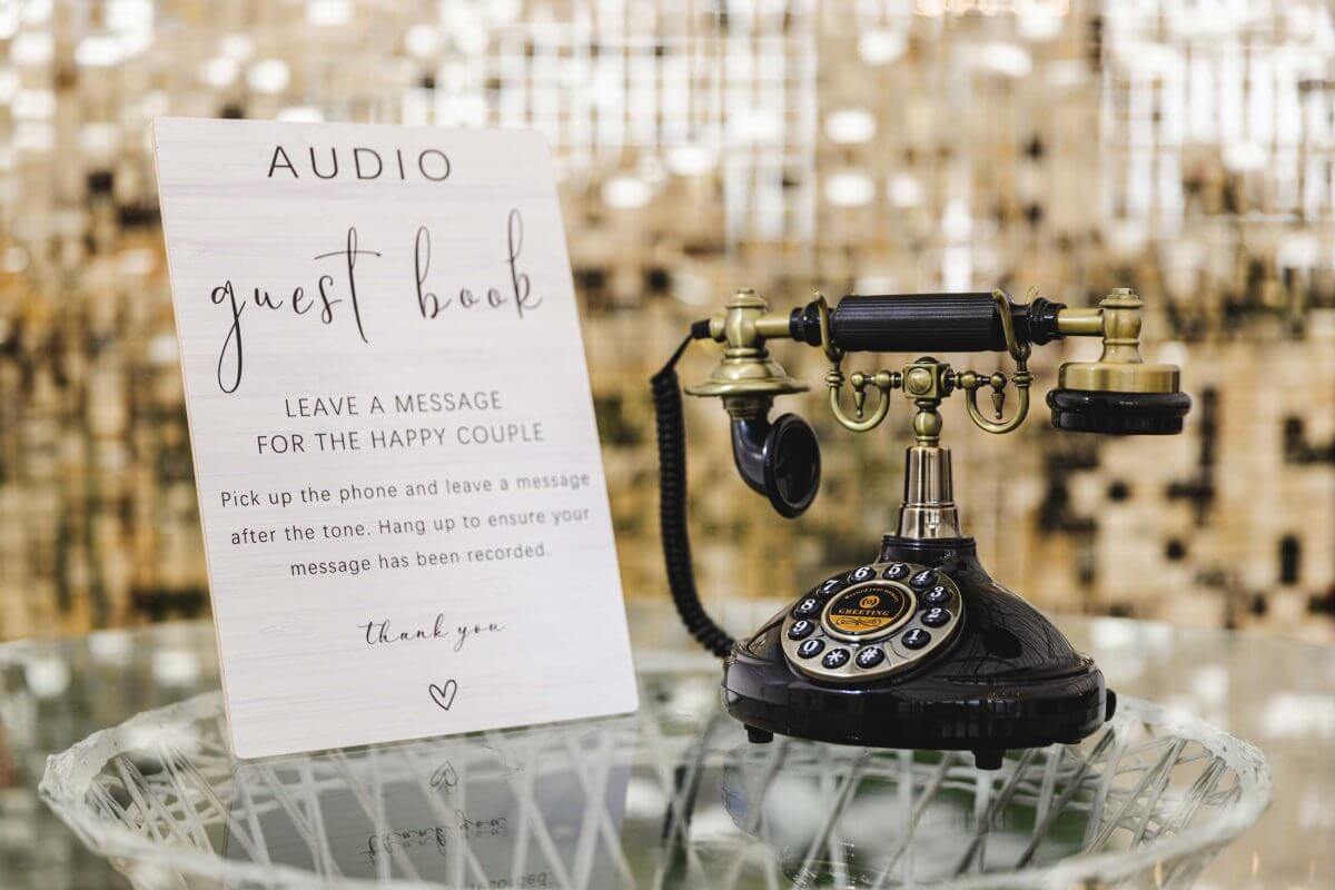 A vintage rotary telephone beside a sign inviting guests to leave an audio message.