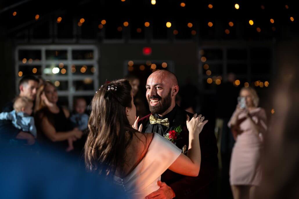 photog-bradt-A7407578 A couple dances together at an indoor event while people watch and take photos. String lights are visible in the background.