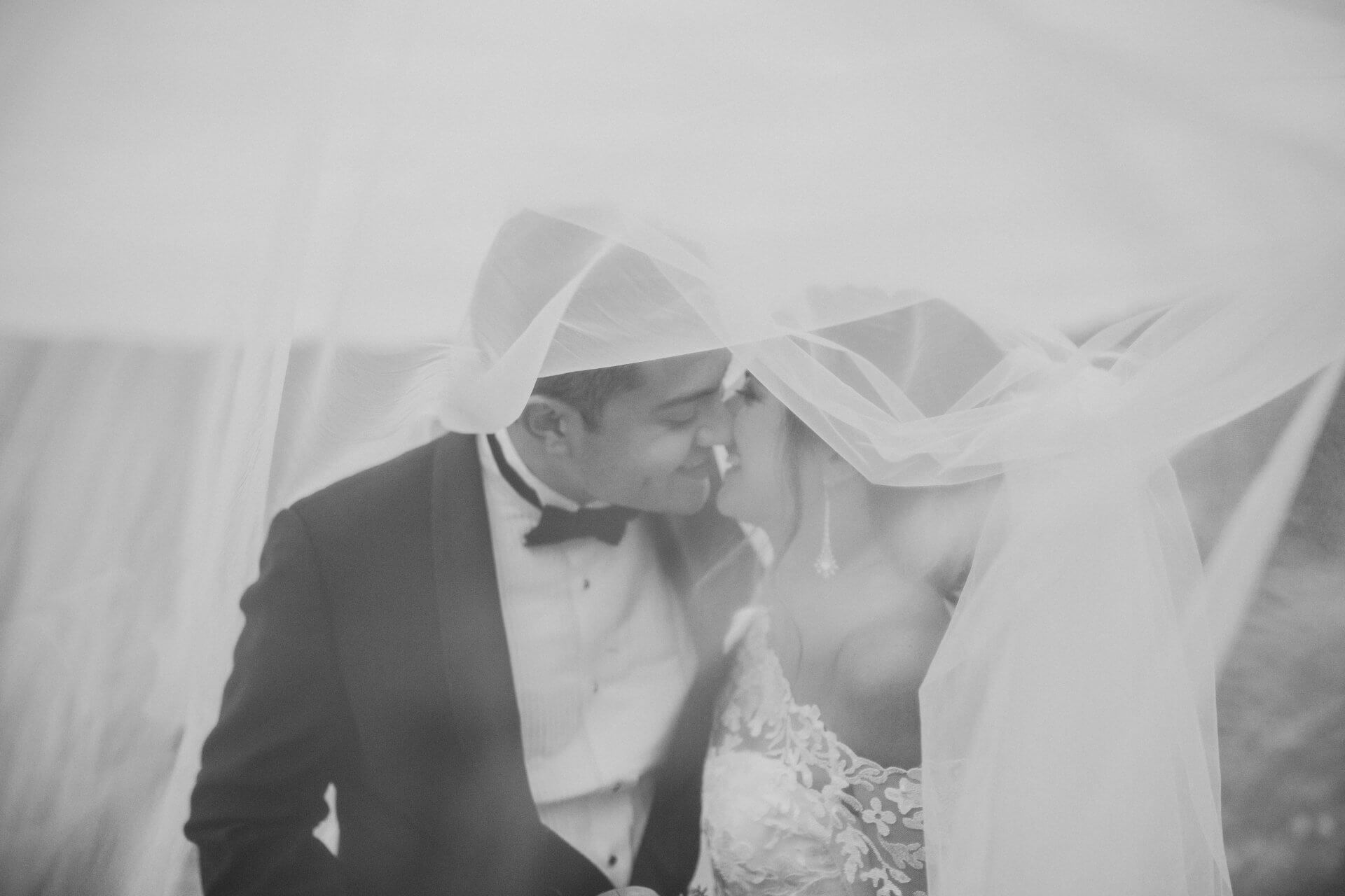 Austin-wedding-photography-ceremony-bride-groom-couple A bride and groom sit close together under a sheer veil, facing each other and about to kiss, on their wedding day.