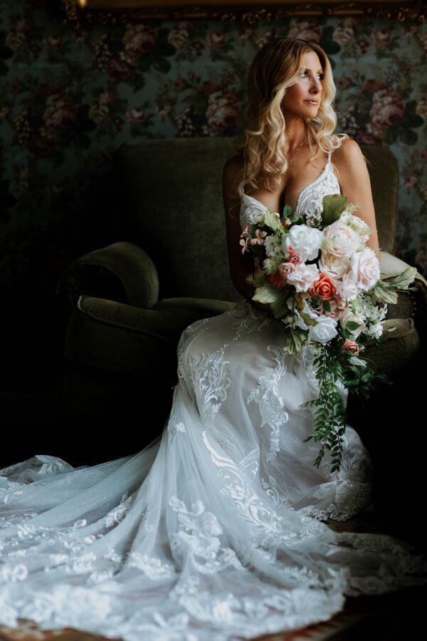 Austin wedding photography by Toast: bride seated in a dark armchair with a pink and white bouquet, in front of floral wallpaper.