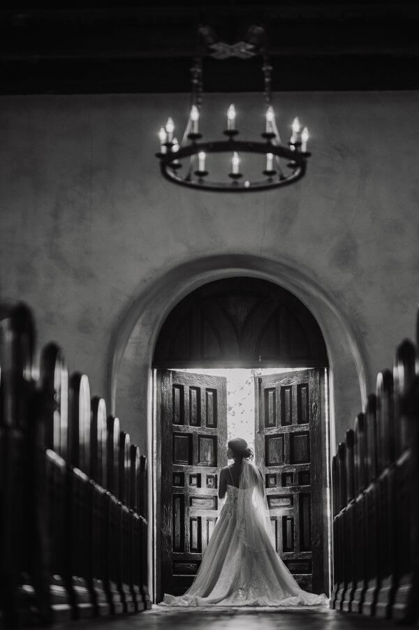 Austin wedding photography by Toast: black and white photo of a bride at open chapel doors, seen from behind past the pews.