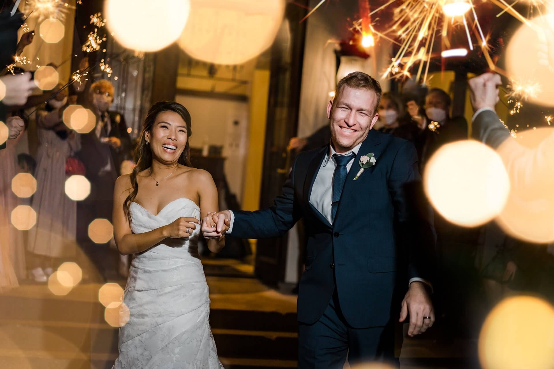 dallas_wedding_exit_bride A bride and groom holding hands and smiling while walking through a crowd with sparklers at night.