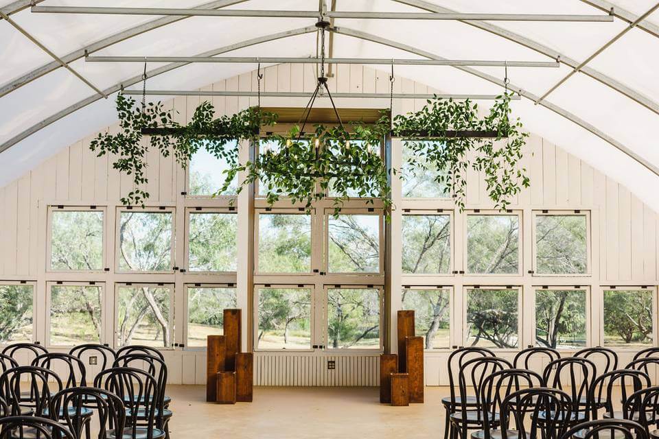 A bright room with large grid windows, rows of black chairs, wood blocks at the front, and green foliage hanging from the ceiling—perfect for those seeking unique wedding venues in Dallas.