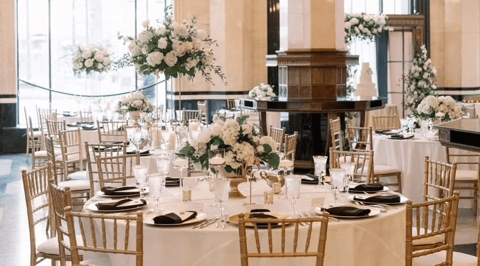 Elegant banquet hall set for an event, featuring round tables with white linens, gold chairs, and flower centerpieces—perfect for those seeking wedding venues in Fort Worth.
