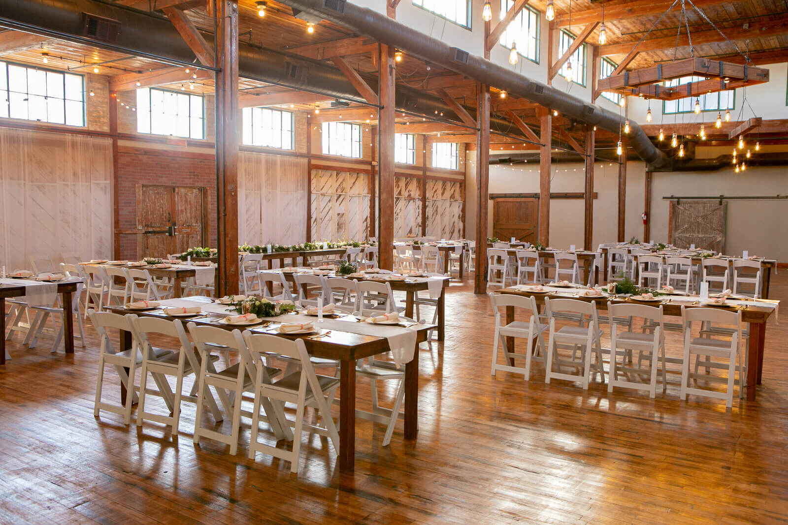 Spacious event hall with wooden floors, high ceilings, and large windows, set up with rectangular tables and white chairs—perfect for gatherings or those seeking wedding venues in Fort Worth.