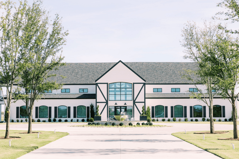 A large modern building with a black and white exterior, tall central windows, and symmetrical design—ideal for wedding venues in Fort Worth—set amid landscaped surroundings with trees and shrubs.