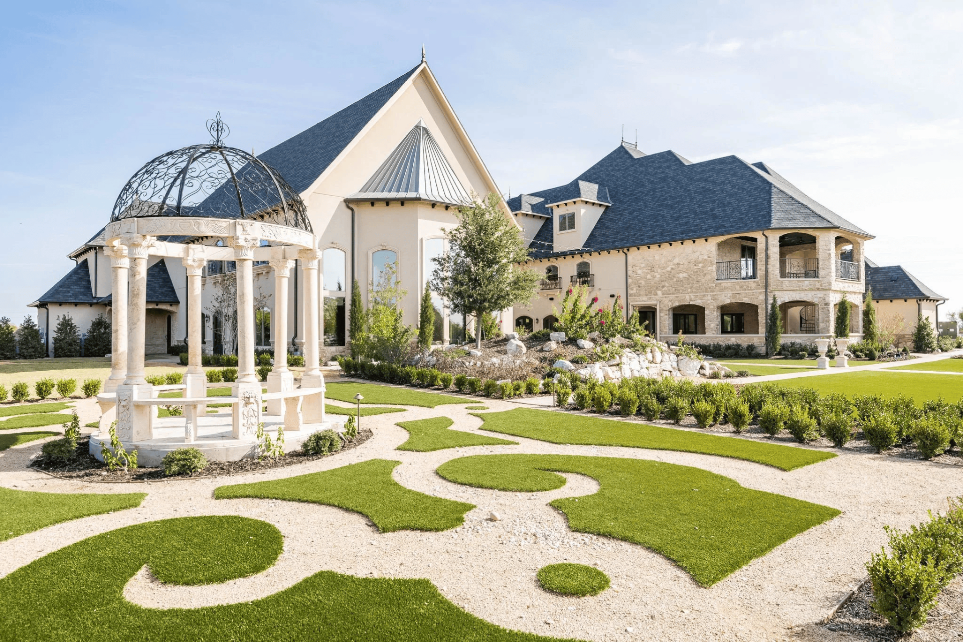 Large stone mansion with multiple peaked roofs, ornate balconies, and manicured lawn featuring a decorative white gazebo and intricate garden paths—an elegant choice among wedding venues in Fort Worth.