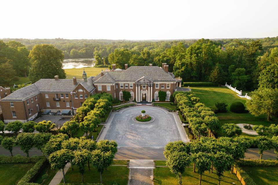 Aerial view of a large, stately mansion with manicured gardens and circular driveway, ideal for wedding venues in Austin, surrounded by trees and set in a lush, green landscape.