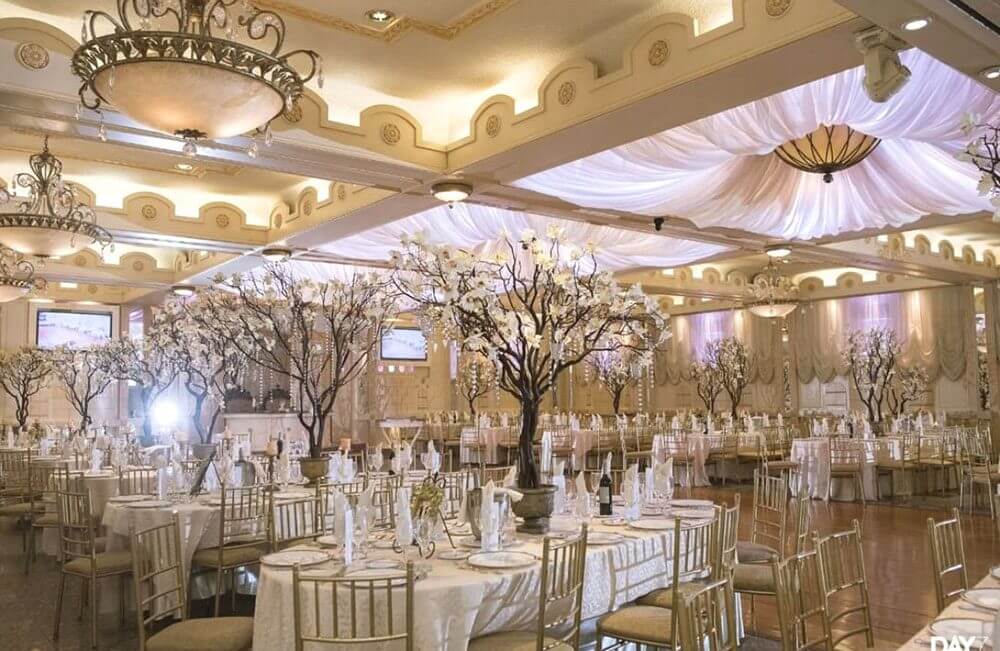 Elegant banquet hall with round tables set for an event, decorated with white floral centerpieces and draped ceiling lights—an ideal setting among wedding venues in Austin.