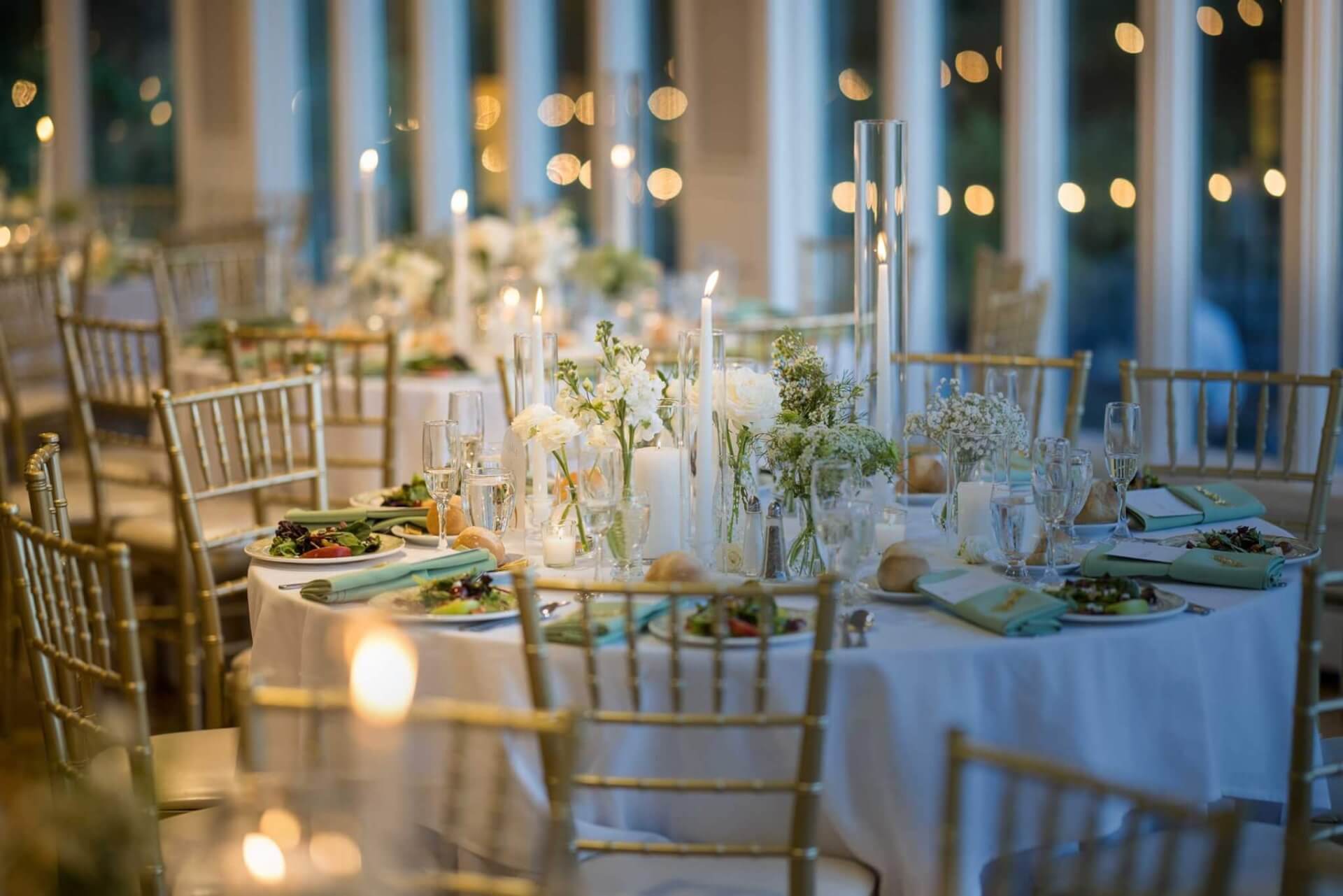 Elegant banquet tables set with white tablecloths, gold chairs, floral centerpieces, and candles create a romantic atmosphere—perfect for those seeking wedding venues in Austin with a softly lit, formal event space.