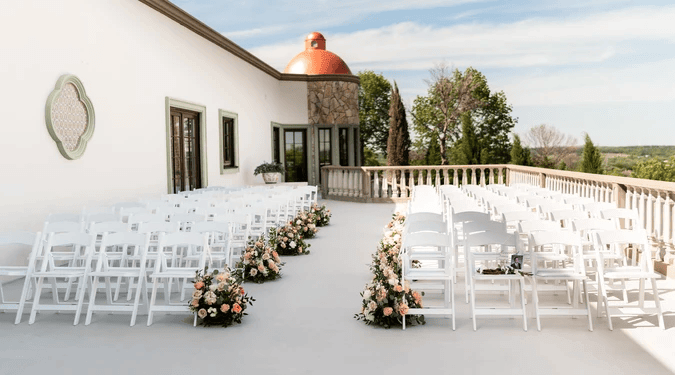 Outdoor wedding ceremony setup with rows of white chairs facing a floral-lined aisle on a scenic balcony with a dome structure—one of the most stunning wedding venues in Fort Worth.