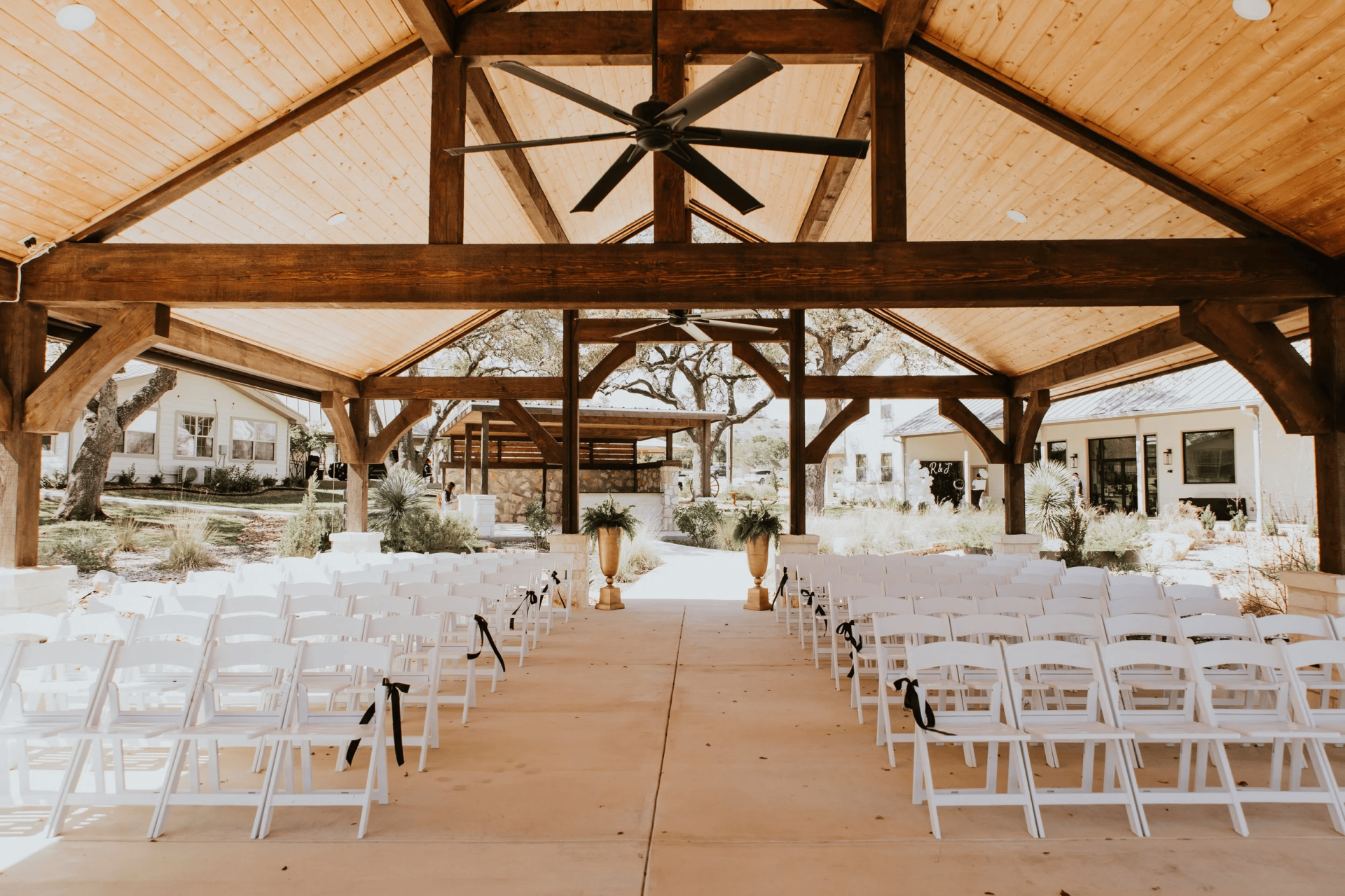 Rows of white chairs are arranged under a wooden pavilion for a ceremony at one of the charming San Antonio wedding venues, with greenery and decorative plants placed at the front.