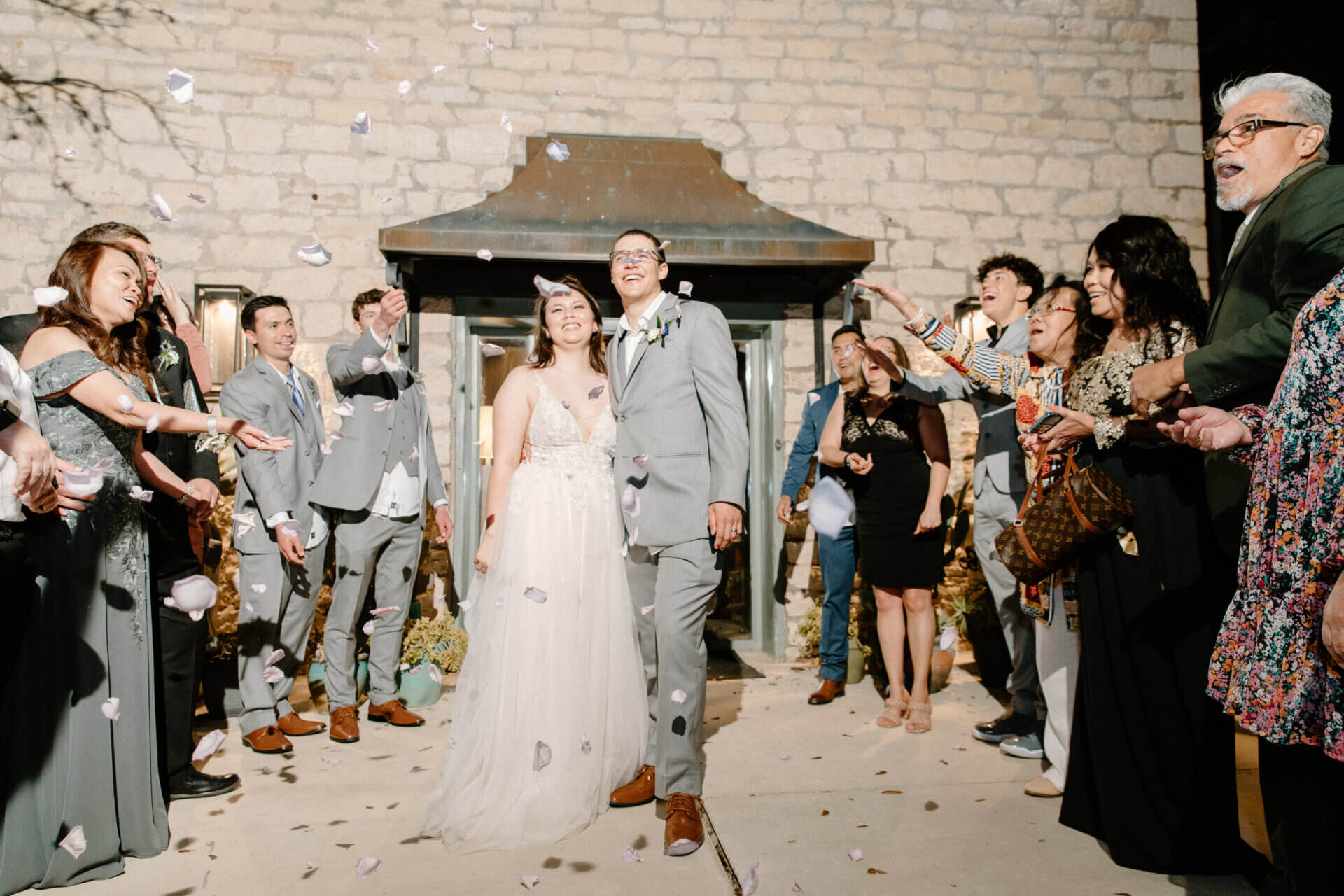 Bride and groom grand exit through petals at the Stonehouse Villa stone house entrance, Driftwood TX wedding venue