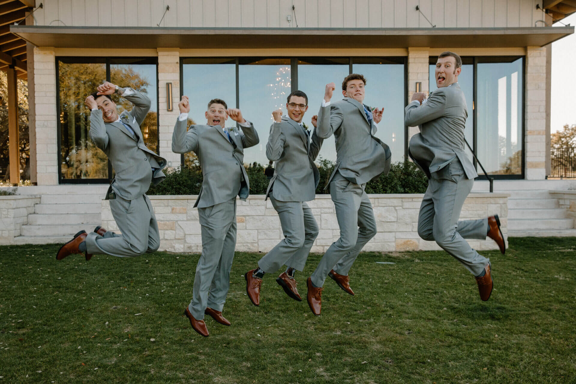 Groomsmen jumping on the lawn outside the Stonehouse Villa Reception Hall, Driftwood TX wedding venue